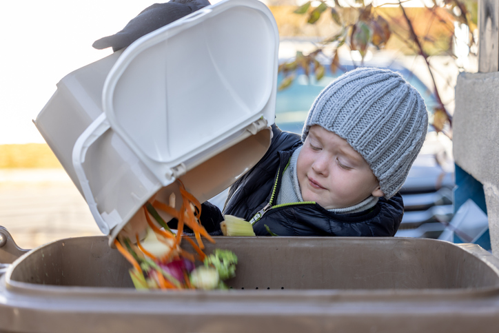 Young student with stocking cap dumps compost into a bin