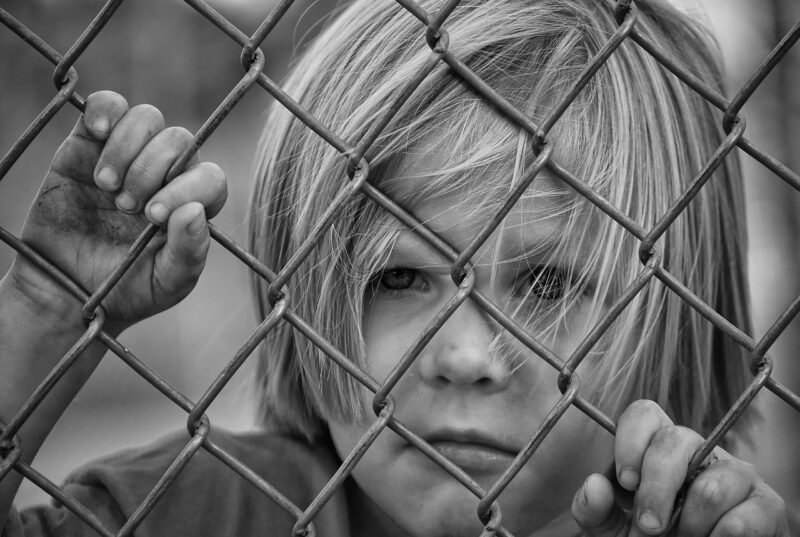 Child with their face pressed up against a wire fence