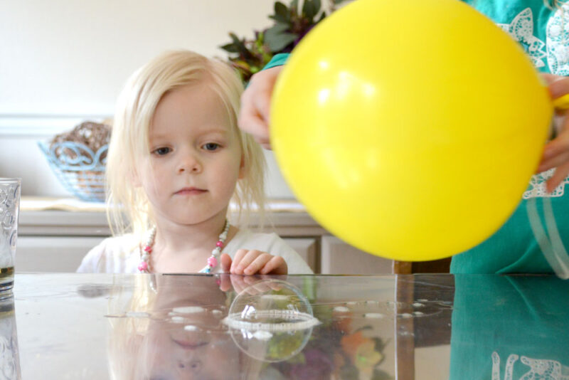 child looking at a bubble on the counter with a balloon for an electricity experiment