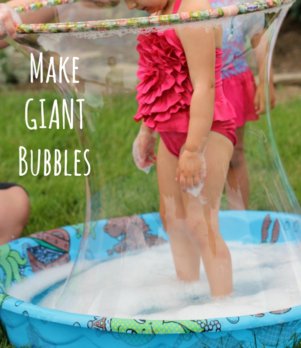 Child standing in a kiddie pool filled with bubbles, while a lifted hula hoop creates a giant bubble around her