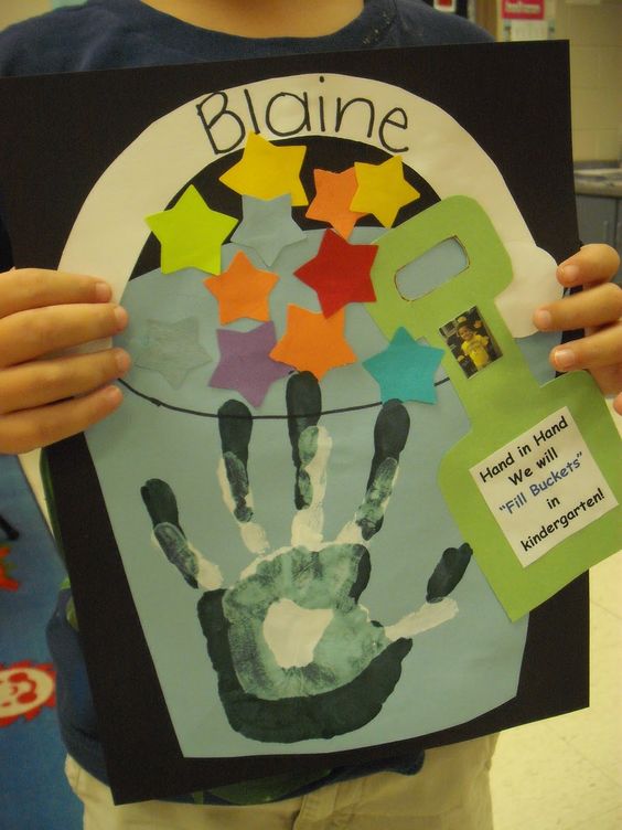 child holding an art project featuring a bucket and a handprint