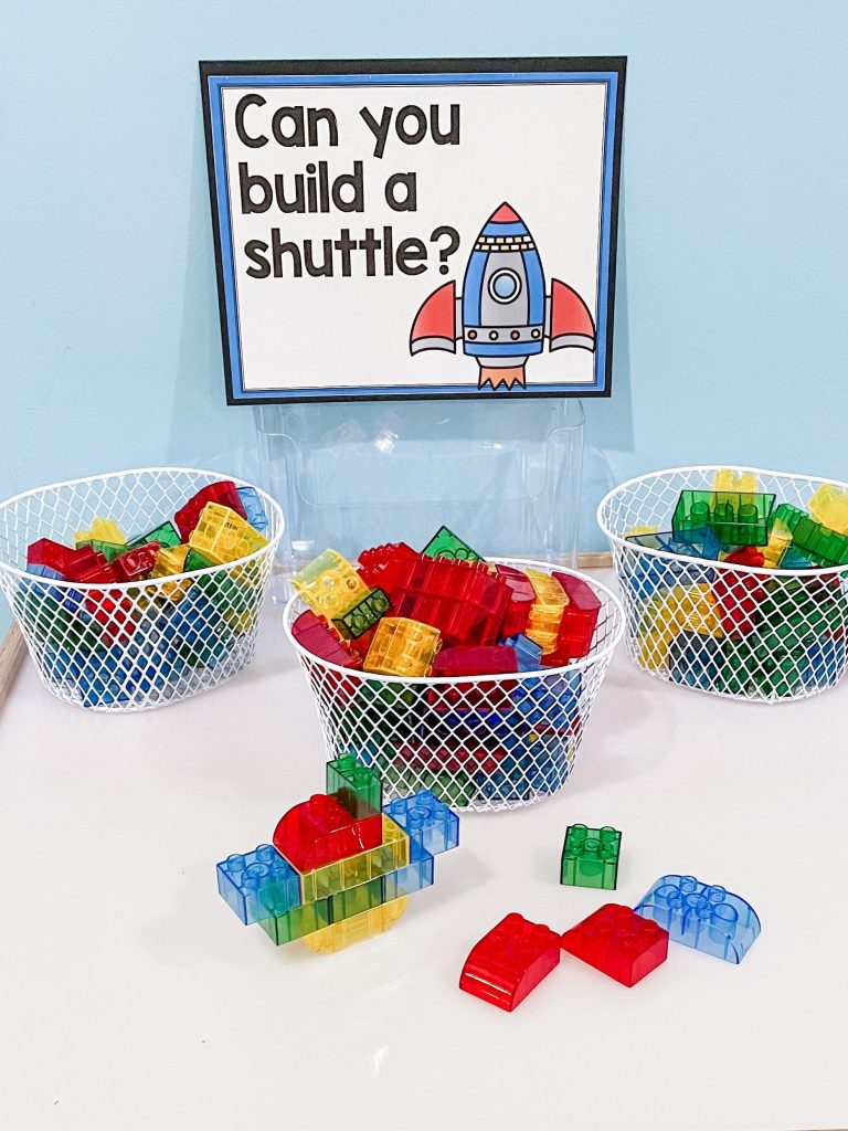 A sign reads Can you build a shuttle? Baskets with blocks are under the sign.- space-themed classroom