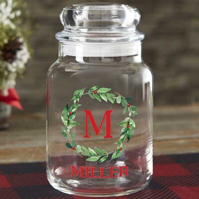 A glass candy jar has a wreath with a letter M in it. It says Miller underneath.