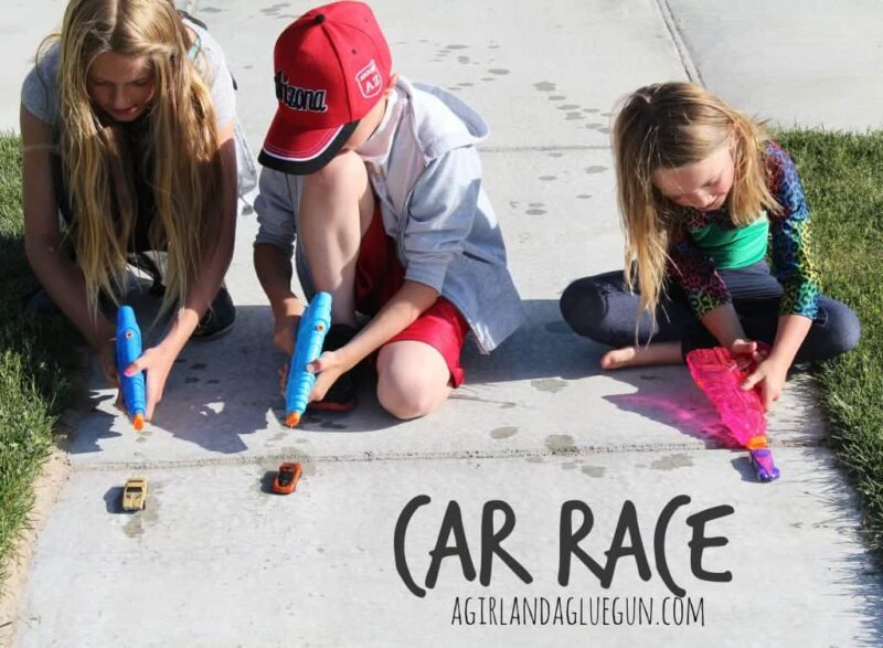 child using squirt gun to push a car down the sidewalk 