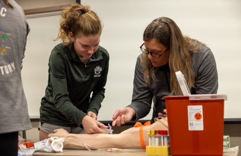Student and health care worker performing a procedure on a model of a human limb