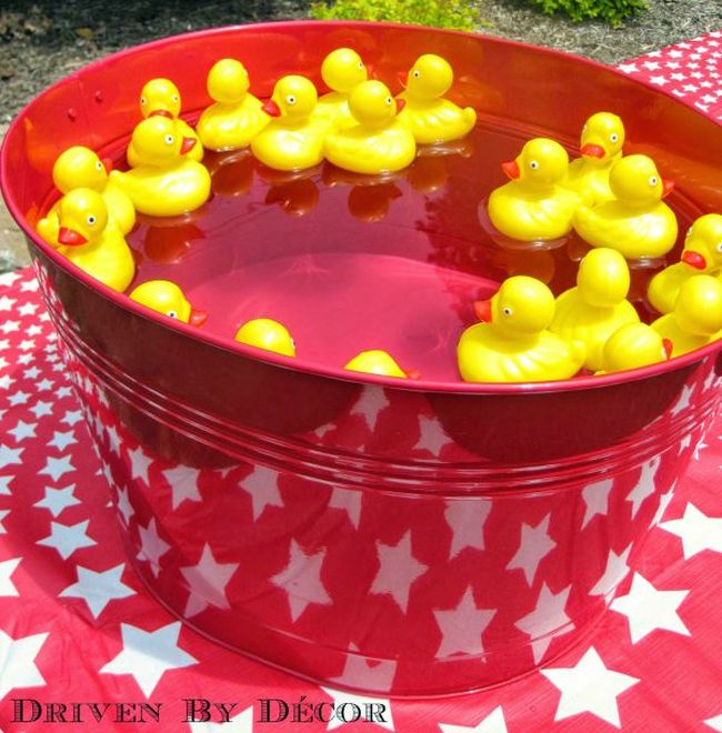 Yellow rubber ducks floating in a large red bucket of water, on a red tablecloth covered with white stars