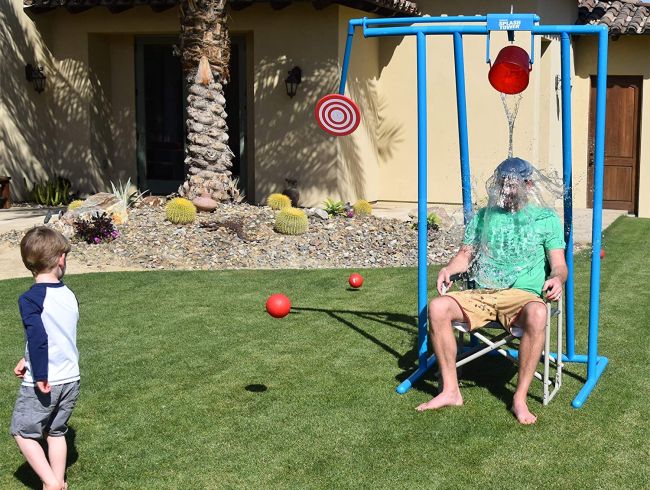 Man being splashed by water from a bucket after a child hits a nearby target with a ball in a carnival games dunk tank