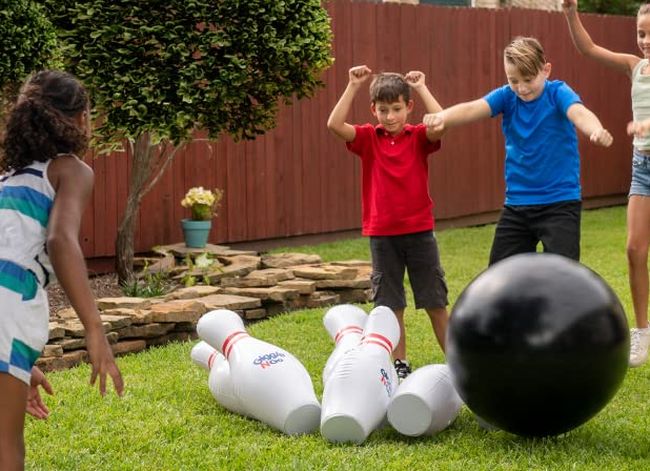 Kids playing with a giant inflatable bowling set outside on a lawn