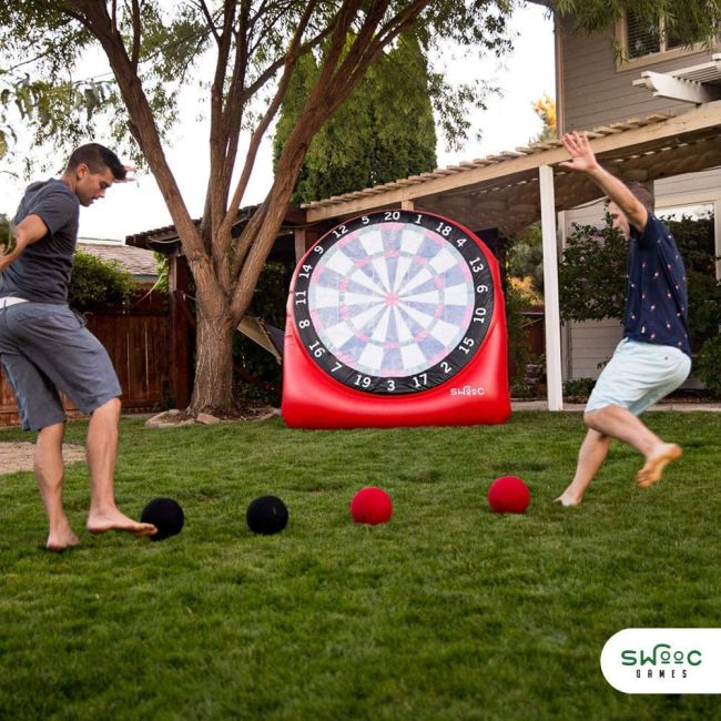 Two men kicking rubber balls at a large inflatable dart board