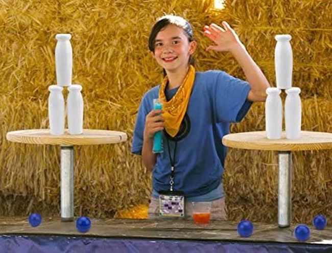 Child posing with stacked milk bottles and small balls for carnival games