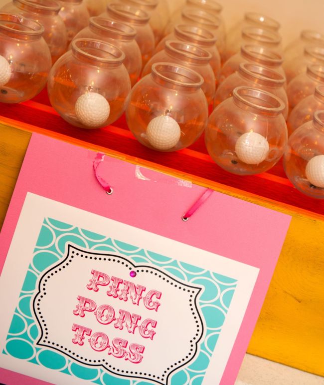 Rows of glass fishbowls with ping pong balls inside, with a sign reading Ping Pong Toss