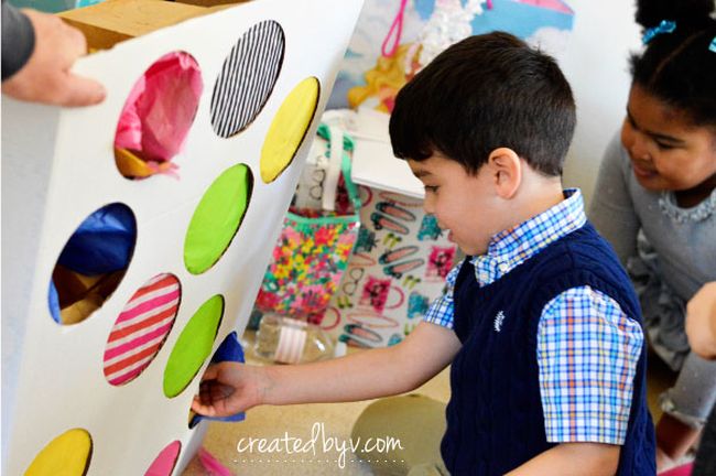 Child punching through a tissue-paper covered circle in a board to pull out a prize for carnival games