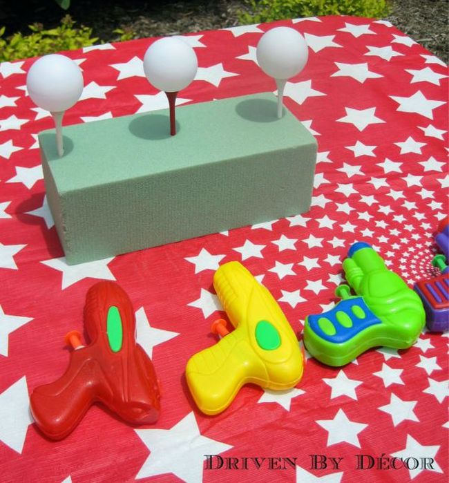 Ping pong balls balanced on golf tees, with three plastic squirt guns for carnival games