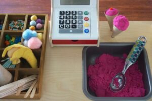 A toy cash register is shown along with play do ice cream with a scoop in it. A try with pretend ice cream toppings is also shown.