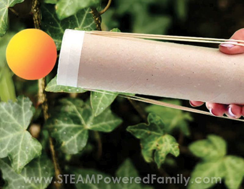 Child using a DIY catapult cannon made from a cardboard tube to launch a ping pong ball