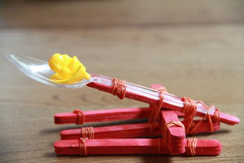 popsicle sticks and elastics are stacked to create a catapult. A plastic spoon makes for the actual catapult piece (preschool science)