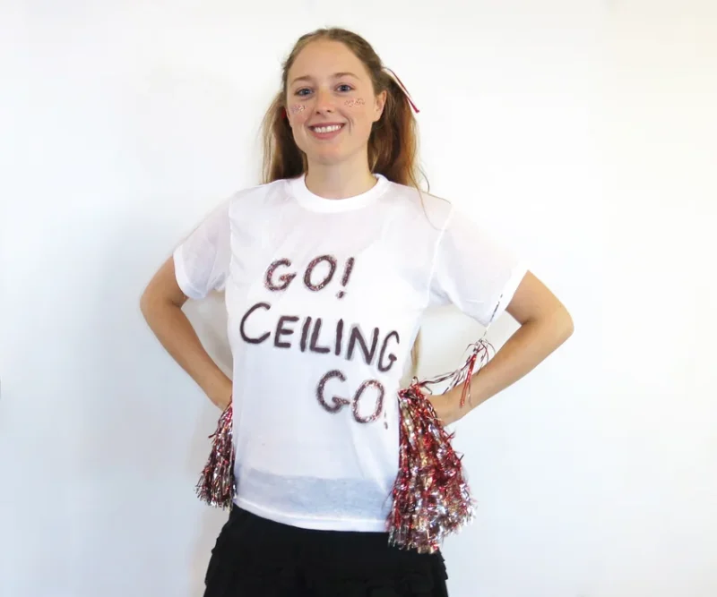 A woman is seen wearing a white shirt that says Go Ceiling Go on it and holding pom poms in this funny teacher Halloween costumes idea.