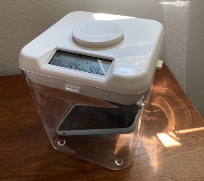 Clear plastic box with white lid with time lock and cell phone inside