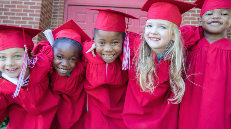 Kindergarten students wearing red graduation caps and gowns
