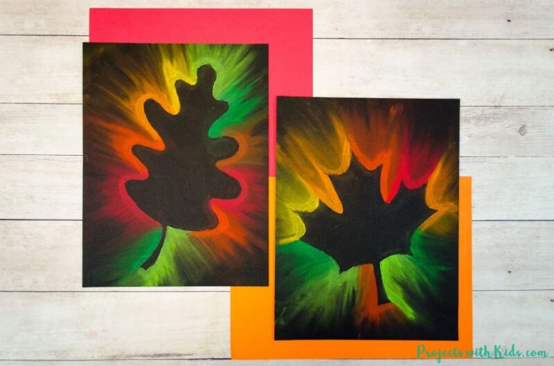 Fall art projects include this one on black paper with leaves on them. The outer edge of the paper is decorated in neon chalk pastels.