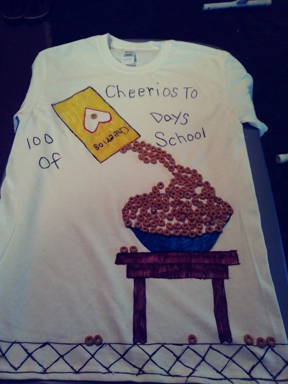 A t-shirt says cheerios to 100 days. It has a cheerios box drawn on it, spilling real cheerios into a bowl.