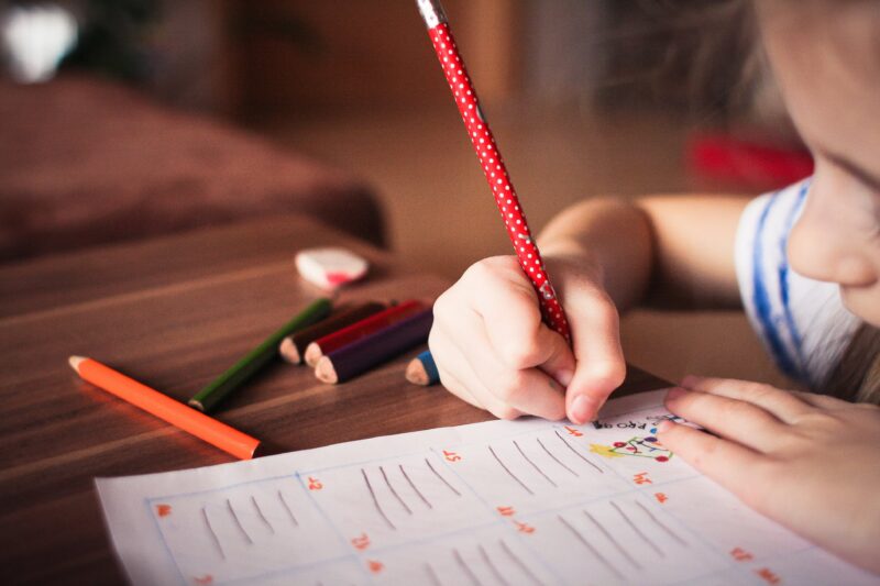 Child writing with a red pencil