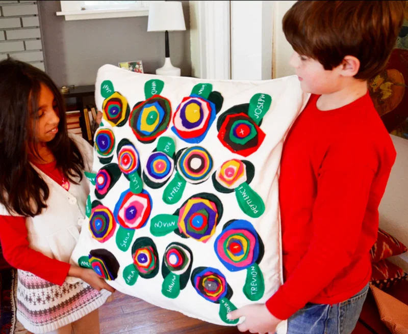 Tow children holding a class pillow made from colorful felt circles and leaves