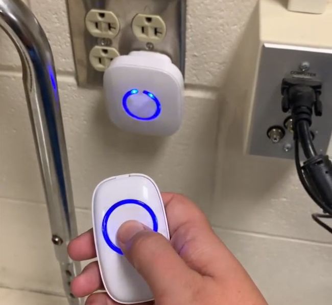 Teacher using a remote to activate a wireless classroom doorbell plugged into an outlet as example of classroom doorbell