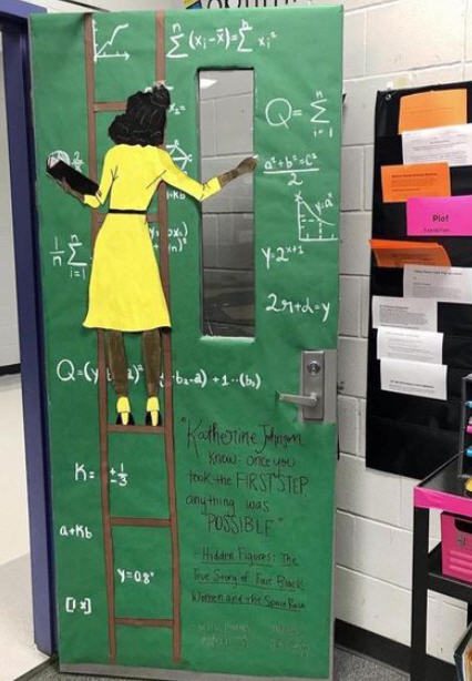 Classroom door showing a Black woman in a yellow dress standing on a ladder, doing math formulas on a chalkboard. 