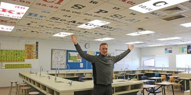 A teacher showing off the ceiling tiles painted like the periodic table of the elements