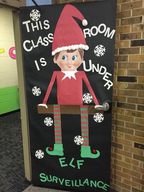 Holiday classroom doors include this one decorated with a large image of an Elf on the Shelf, with text reading This classroom is under elf surveillance"