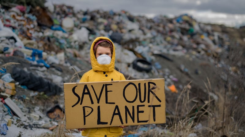 Child in raincoat in front of dump with Save Our Planet sign
