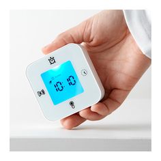 A hand is shown holding a small white square timer/clock/thermometer.