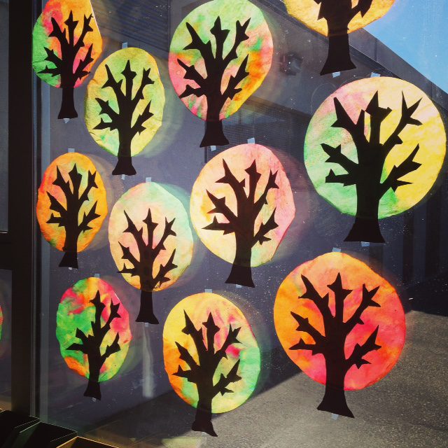 12 trees are shown as black silhouettes with colorful circles behind them that are made from coffee filters.