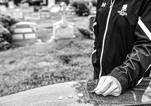 person putting coins on a headstone of a veteran 