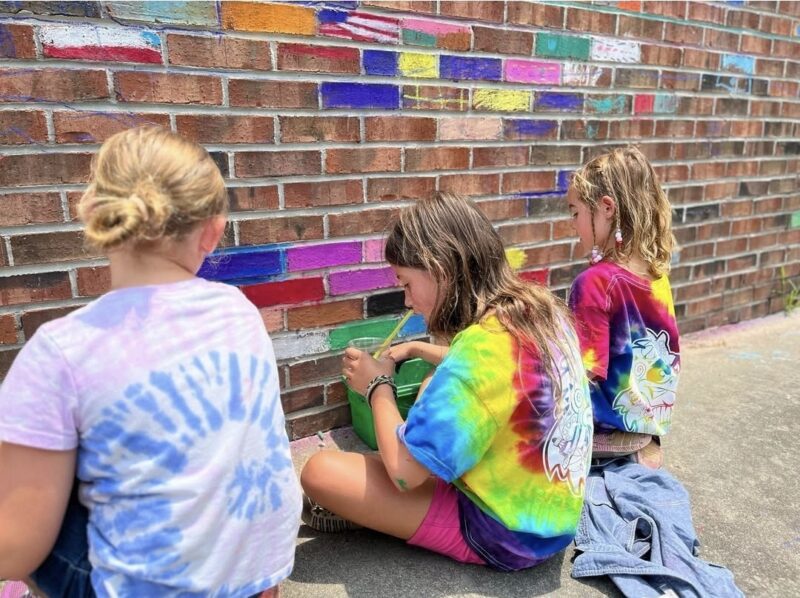 Students using chalk to color individual bricks on a wall