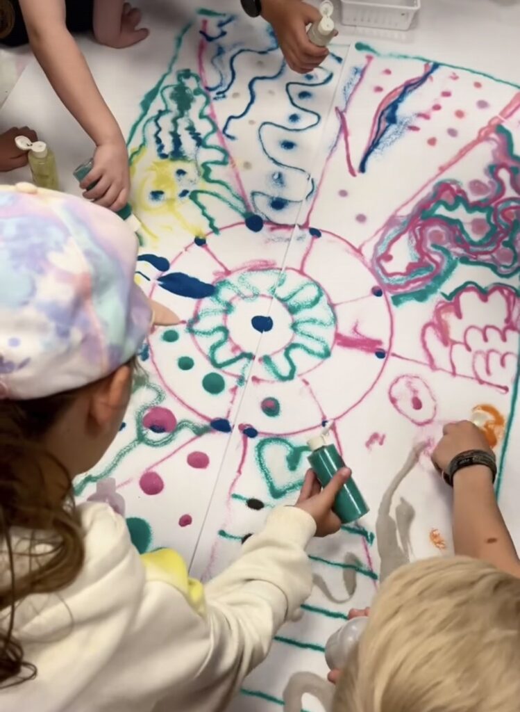 Children using bottles of colored sand to create a mural together