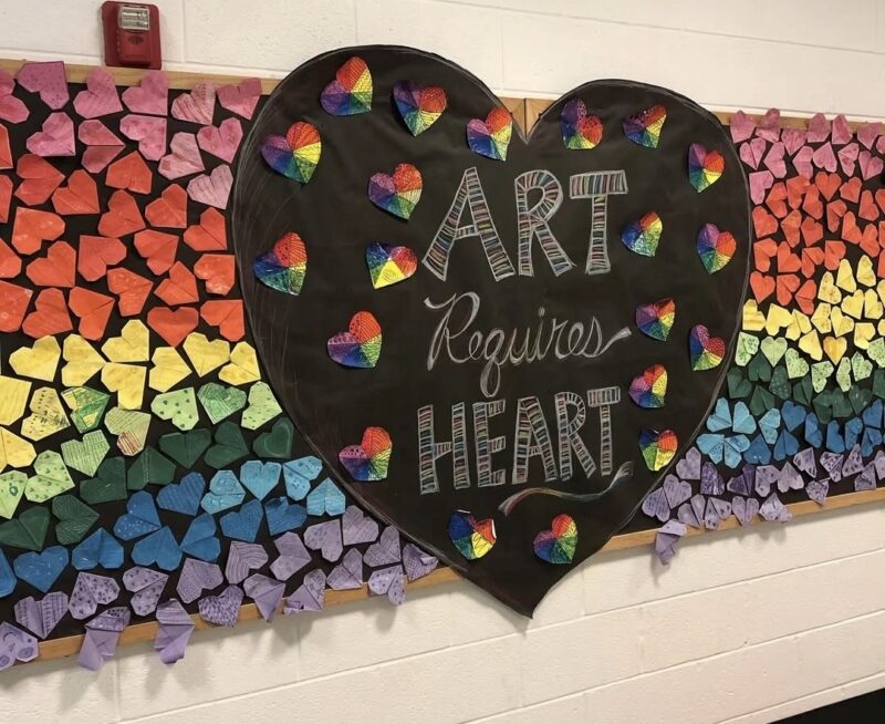 Rainbow of paper origami hearts arranged around a heart reading Art Requires Heart