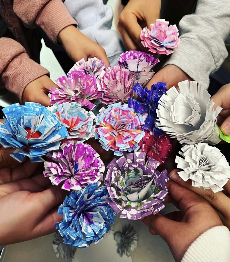 Students holding individual paper flowers to form a collaborative bouquet