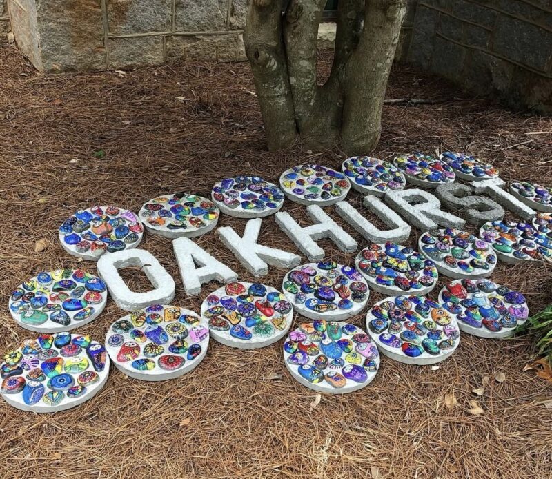 Individually painted river rocks made into cement stepping stones, arranged around cement letters spelling out Oakhurst
