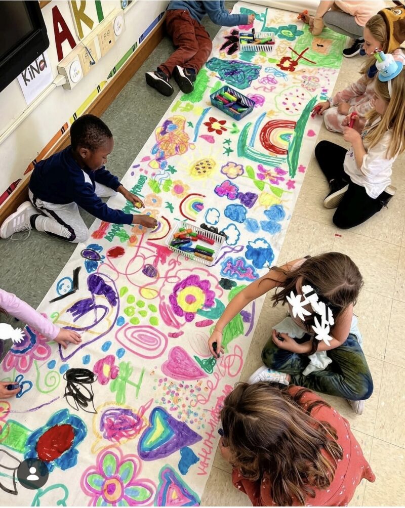 Children using paint markers to create a large colorful mural together