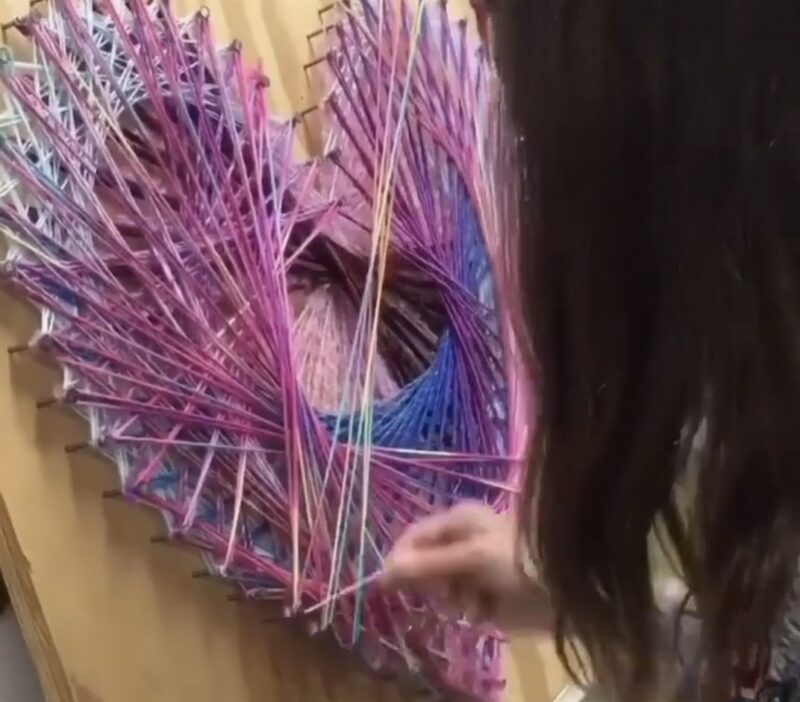 Student looping purple yarn around nails arranged in a heart shape
