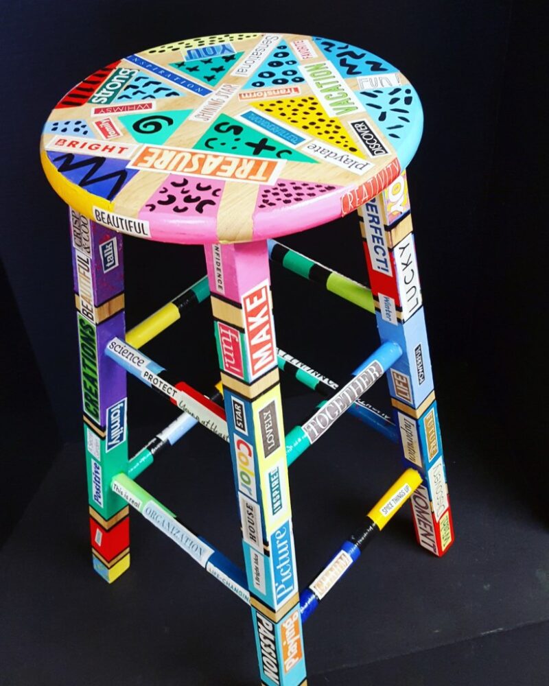 A stool is covered in different patterns and cut out words in this collaborative art project.
