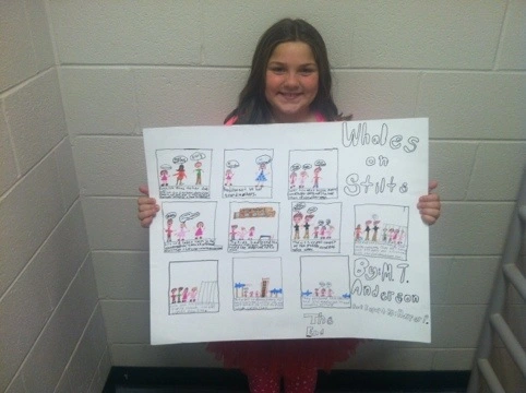 A girl stands holding a comic strip book report as an example of creative book report ideas
