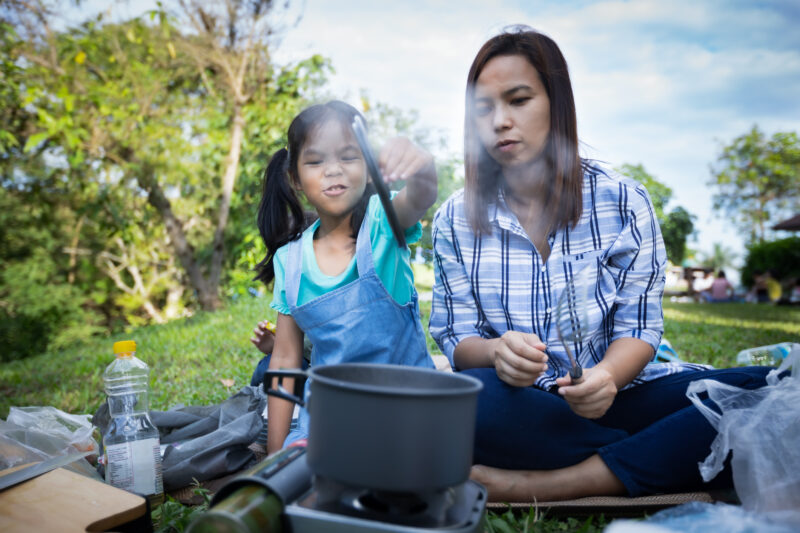 Cute Asian child girl having fun to help her mother cooking while camping with family, as an example of camping activities for kids.