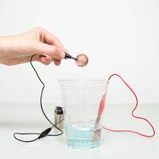 a hand holding copper penny above water with wires going into the wire 