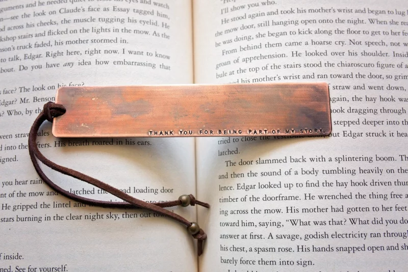 Copper stamped bookmark with leather tassel on an open book that says, "Thank you for being part of my story."