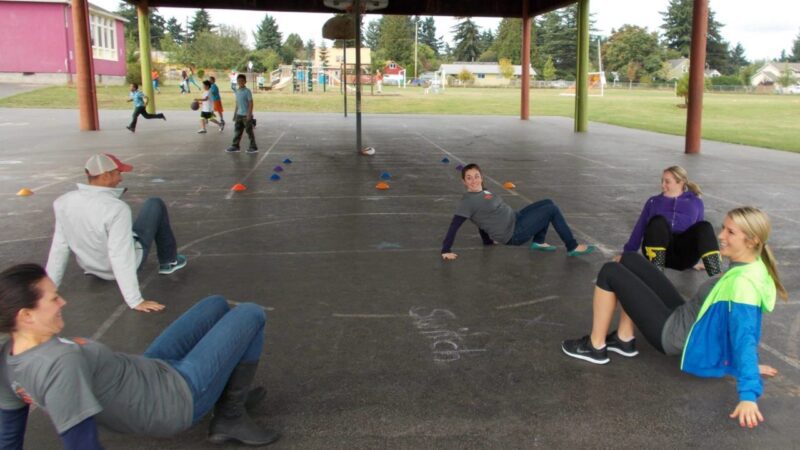 People are shown on all fours ready to kick a ball while imitating crabs (elementary PE games)