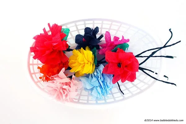 A glass plate has a variety of flowers on it which are made from crepe paper.