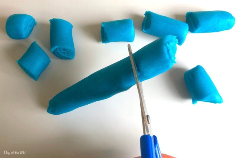 A child uses scissors to cut through play dough